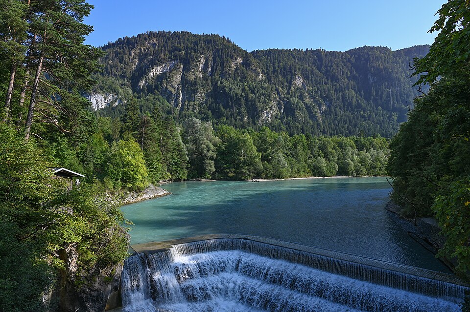 The Lech river pouring over the stepped Lechfall weir below wooded cliffs near Füssen.