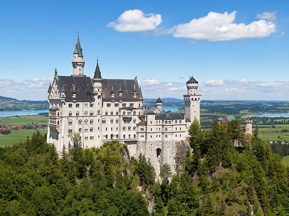 Schloss Neuschwanstein on its wooded ridge with the Forggensee and the Alpine foreland behind.