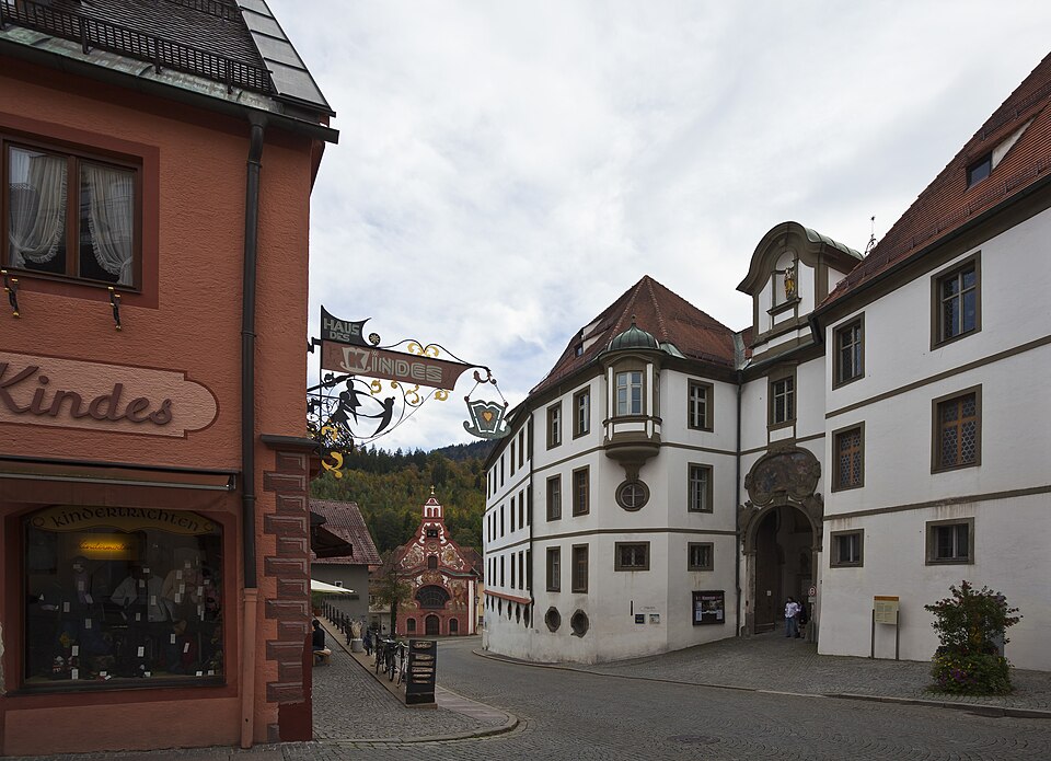 The white Baroque facade of the former St. Mang abbey on a street in Füssen's old town.